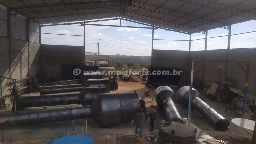 Foto interna do galpão da MAISFORTE com 6 caixas d'água metálicas sendo fabricadas todas do tipo taça, alguns bebedouros e todas as caixas ainda sem pintura.