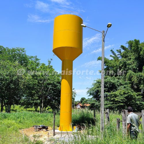 caixa d'água tipo taça coluna seca cor amarela instalada em fazenda com arvores verdes ao redor e um rapaz de costas observando a caixa d'água